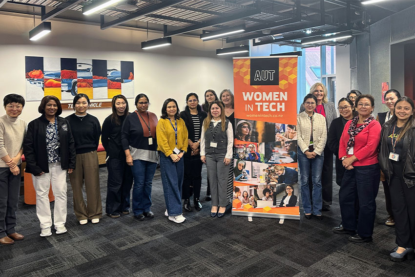 Women in tech stand together (next to a pull-up banner)